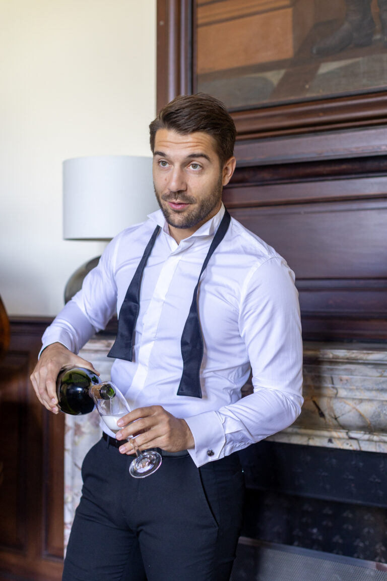 préparatifs Gabriel : mariage Lola et Gabriel Château de la baronnie Gabriel est debout et pose à côté du piano à queue, il sert le champagne à ses témoins