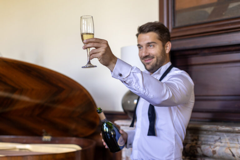 préparatifs Gabriel : mariage Lola et Gabriel Château de la baronnie Gabriel est debout et pose à côté du piano à queue, il sert le champagne à ses témoins