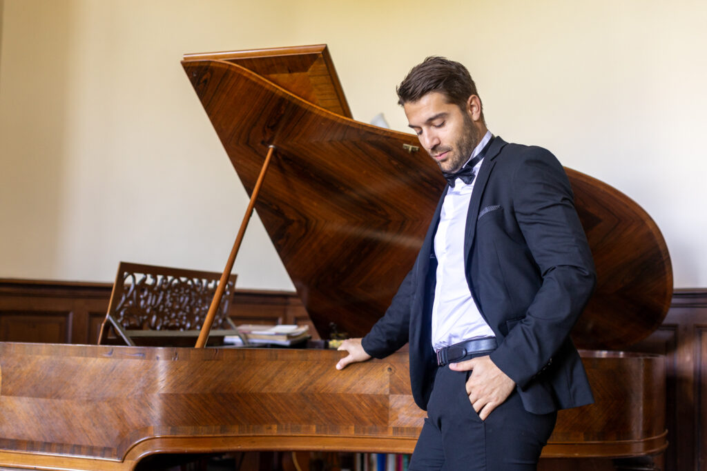 préparatifs Gabriel : mariage Lola et Gabriel Château de la baronnie Gabriel est debout et pose à côté du piano à queue
