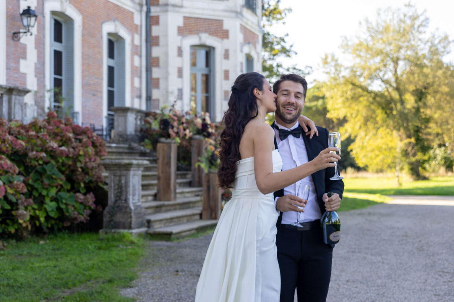 Mariage Lola et Gabriel Château de la baronnie, Lola et Gabriel sont devant le chateau et s'embrasse autour d'une coupe de champagne