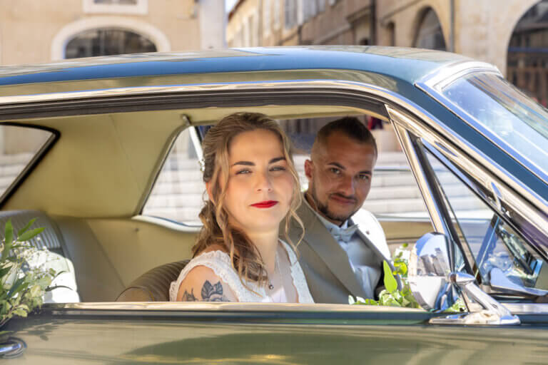 Couple de jeunes mariés posant dans une Mustang blanche devant la cathédrale Sainte-Marie d’Auch le jour de leur mariage