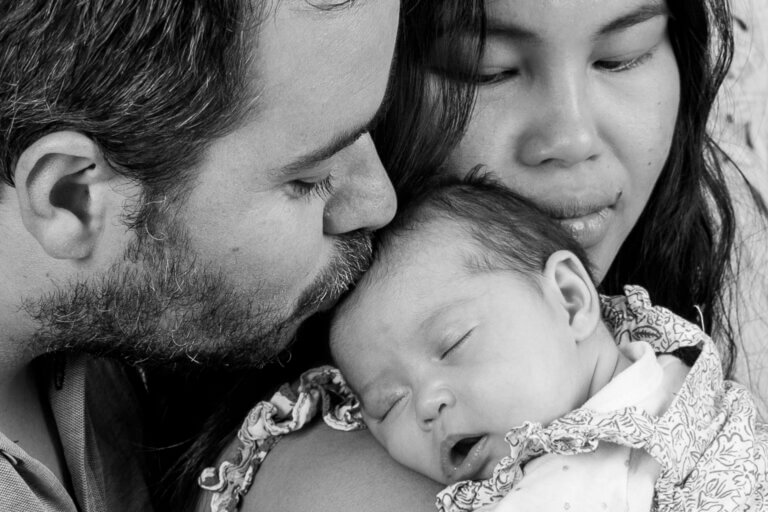 Photo en noir et blanc d’un couple tenant leur bébé dans leurs bras, en studio