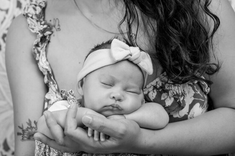 Photo en noir et blanc d’une maman tenant tendrement sa petite fille dans ses bras, en studio