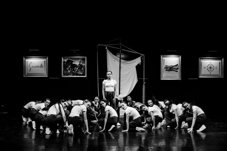 Groupe de danseuses sur scène, en mouvement, toutes synchronisées dans une chorégraphie contemporaine