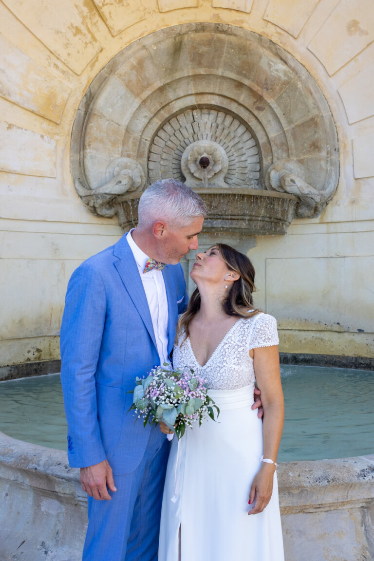 Couple de mariés échangeant un regard amoureux devant la fontaine de l’Escalier Monumental