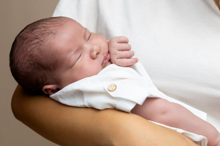 Nouveau-né endormi paisiblement dans les bras d’un parent pendant une séance photo.