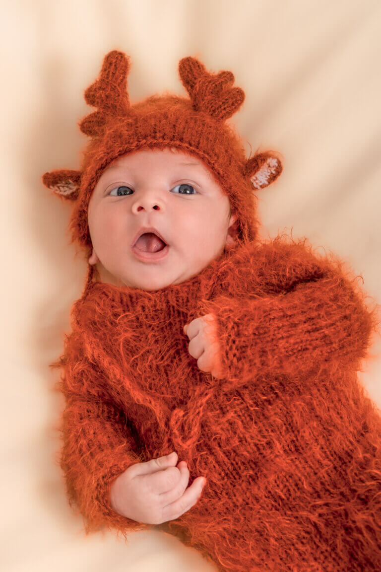 Bébé éveillé portant une tenue marron avec bonnet à petites oreilles et bois de renne.