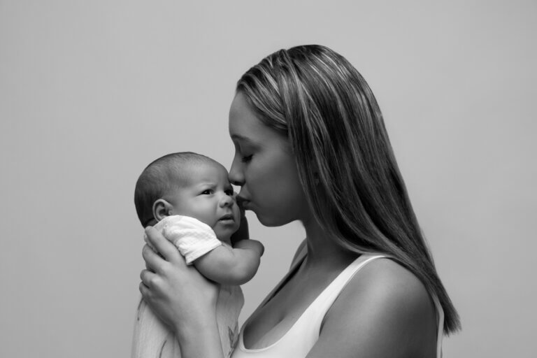 Portrait en noir et blanc d’une maman tenant son nouveau-né et lui donnant un tendre baiser.