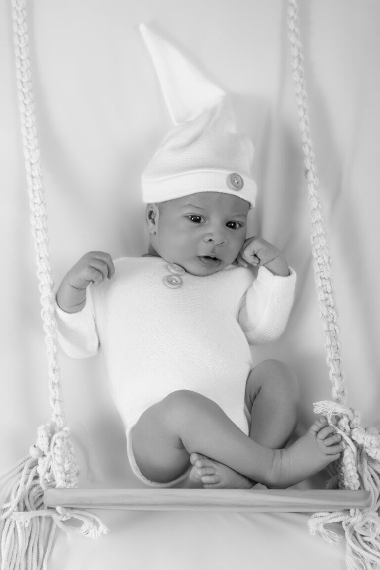 Bébé portant une tenue blanche photographié dans une petite balançoire en macramé en noir et blanc.