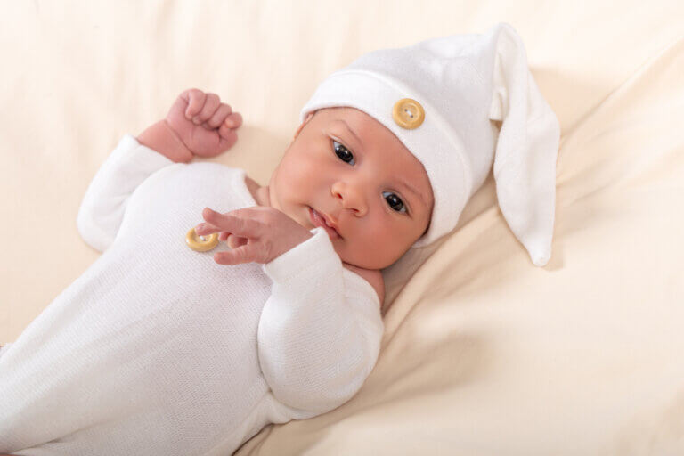 Portrait d’un bébé éveillé portant une tenue blanche et un bonnet lors d’une séance photo à Auch.
