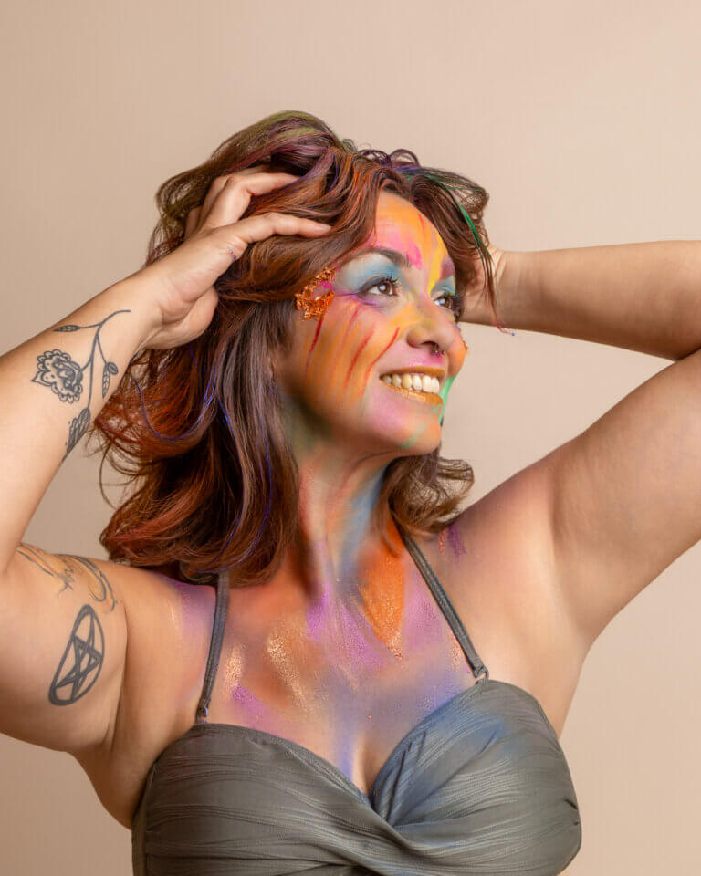 Portrait créatif en studio d’une femme souriante avec un maquillage artistique très coloré.