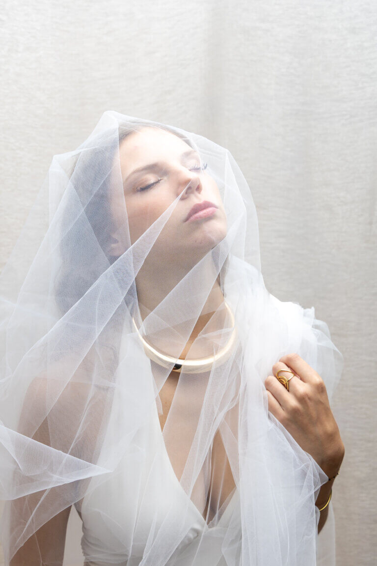 Portrait artistique d’une femme enveloppée dans un voile blanc transparent, les yeux fermés.
