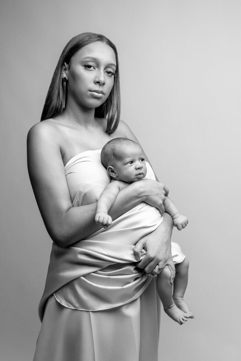 Portrait en noir et blanc d’une maman tenant son bébé dans ses bras lors d’une séance naissance en studio.