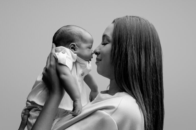Portrait en noir et blanc d’une maman tenant son nouveau-né contre elle, leurs nez se touchant.