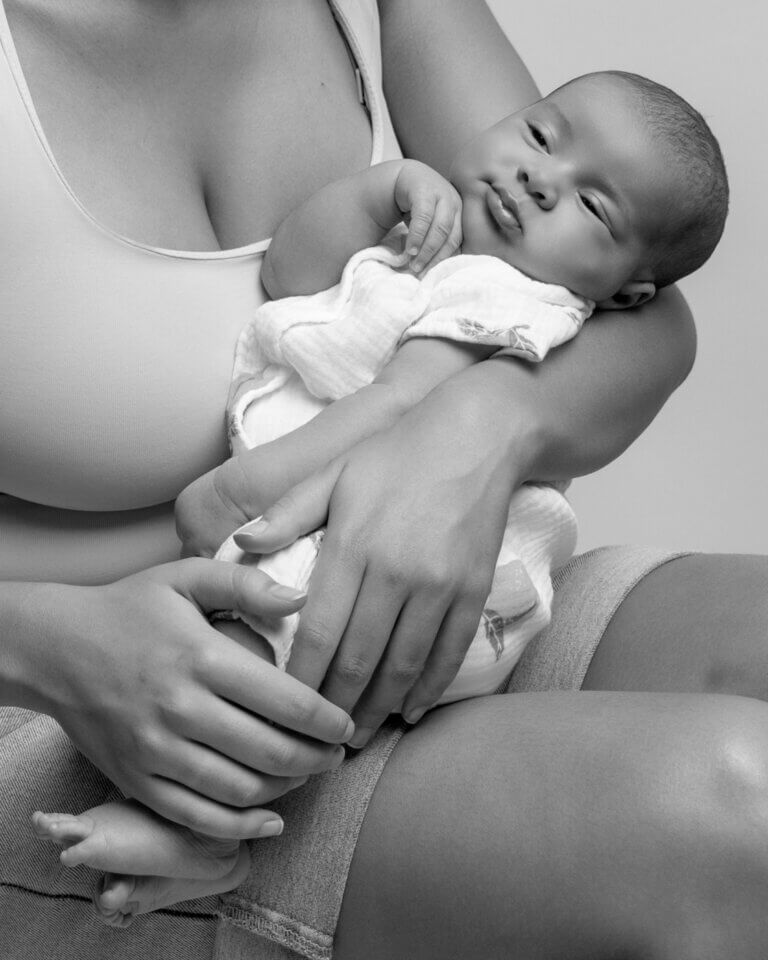 Portrait en noir et blanc d’un nouveau-né éveillé installé dans les bras de sa maman.