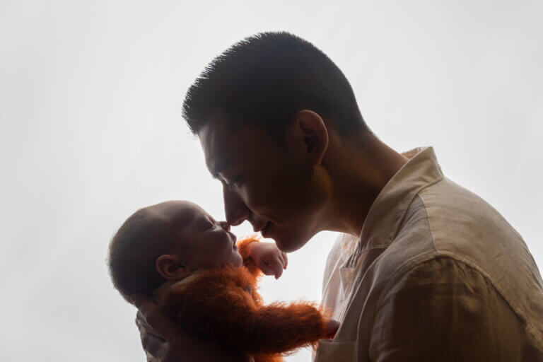 Papa tenant son nouveau-né face à lui pendant une séance photo naissance en studio.