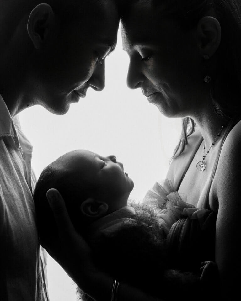 Portrait artistique en noir et blanc de deux parents regardant leur nouveau-né entre eux.