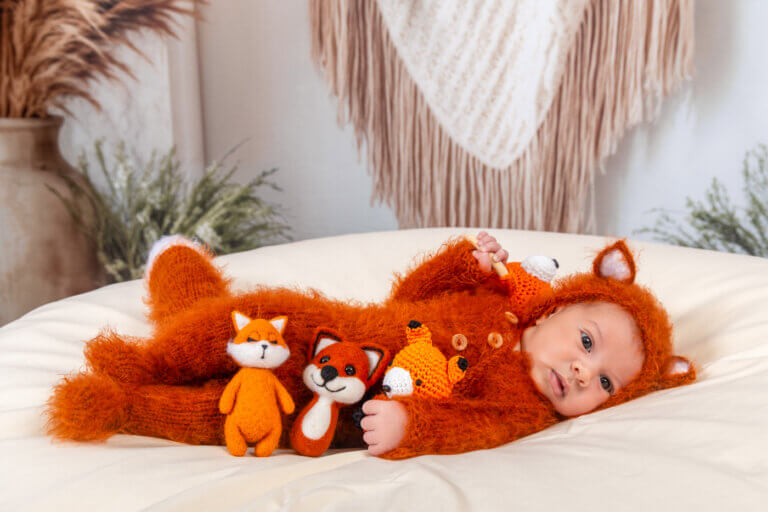 Bébé photographié dans un décor sur le thème du renard avec une tenue orange et des petits renards.
